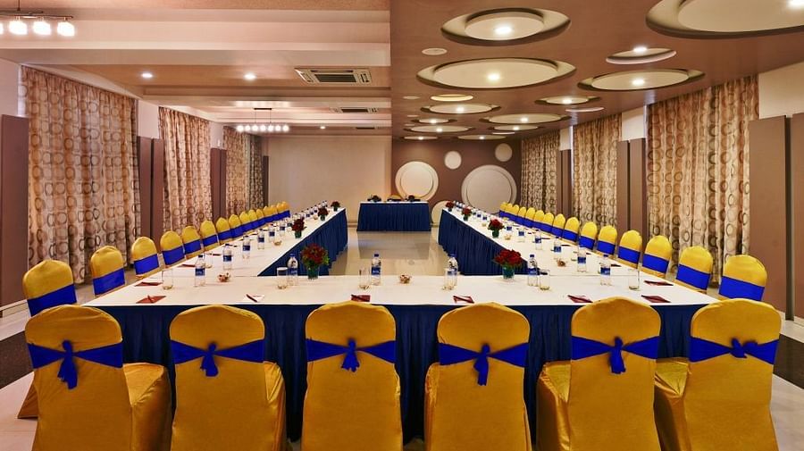 A formal meeting room setup at Lords Inn Porbandar, with a U-shaped table and chairs adorned with blue and yellow sashes.