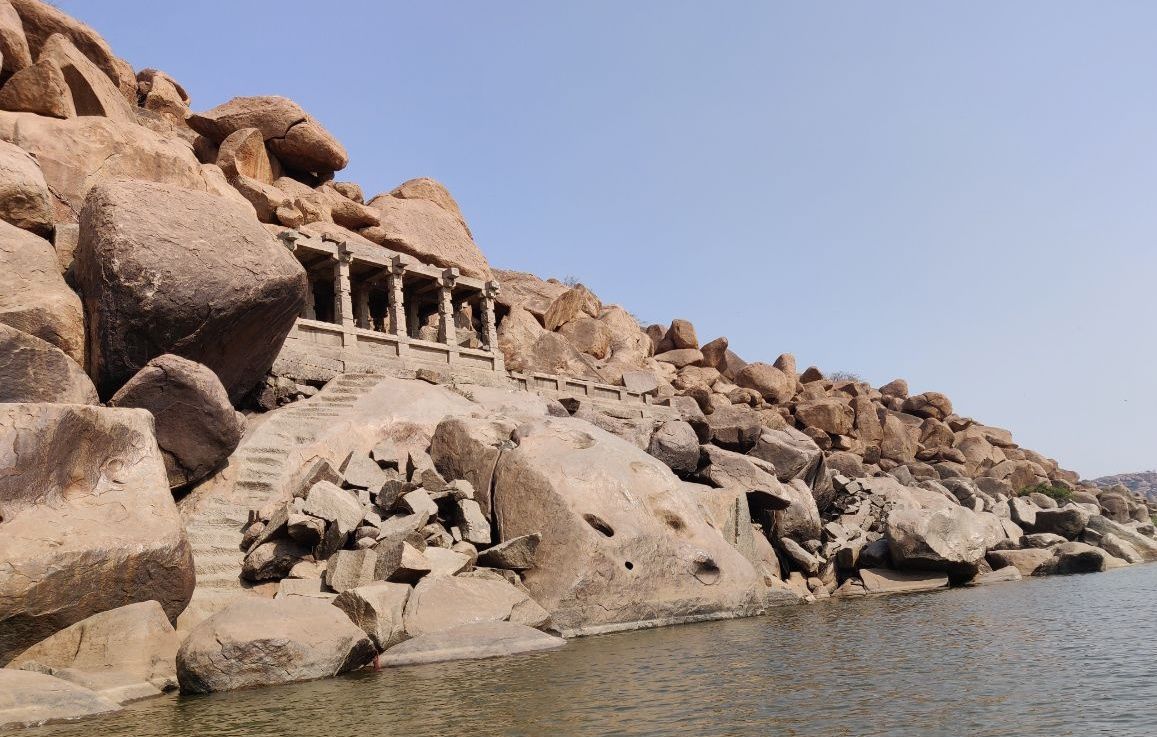 Temple ruins built into rocky hills beside a Hampi river.