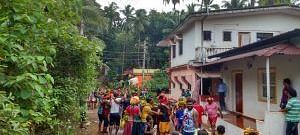 A group of people are gathered on a path between lush green trees and houses.