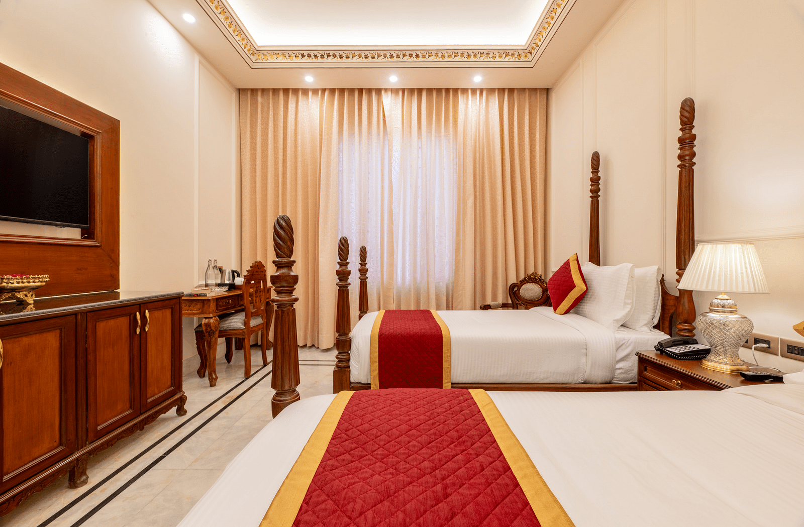 a beautiful room with rajasthani charm featuring two single beds along with beige curtains drawn over the window - Brij Castle, Jaipur