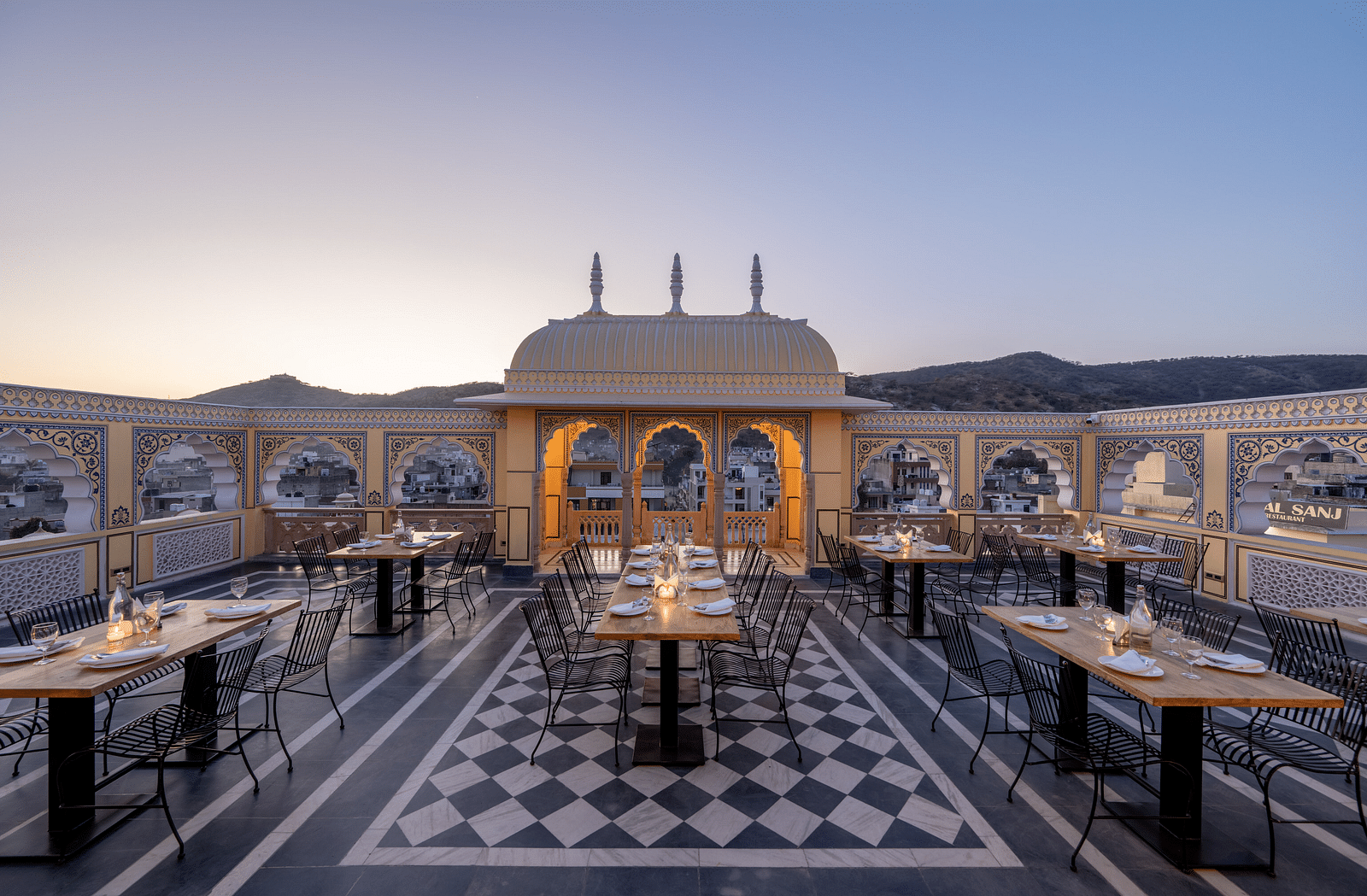a roof top dining setup with beautiful views of the surrounding mountains and the early sunset - Brij Castle, Jaipur