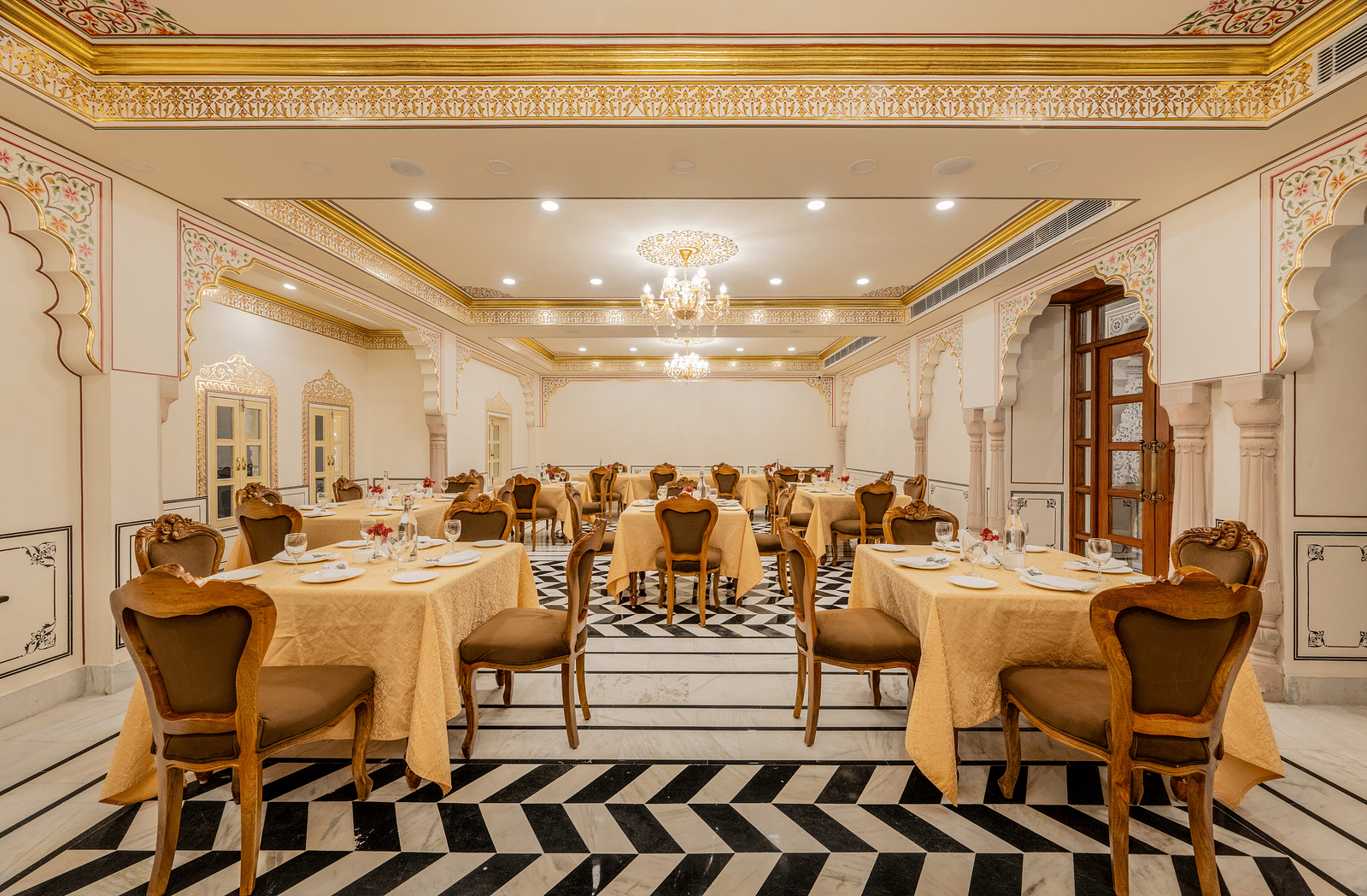 a well arrnaged dining setup in our indoor restaurant with black and white tiles and elegant furnishings - Brij Castle, Jaipur