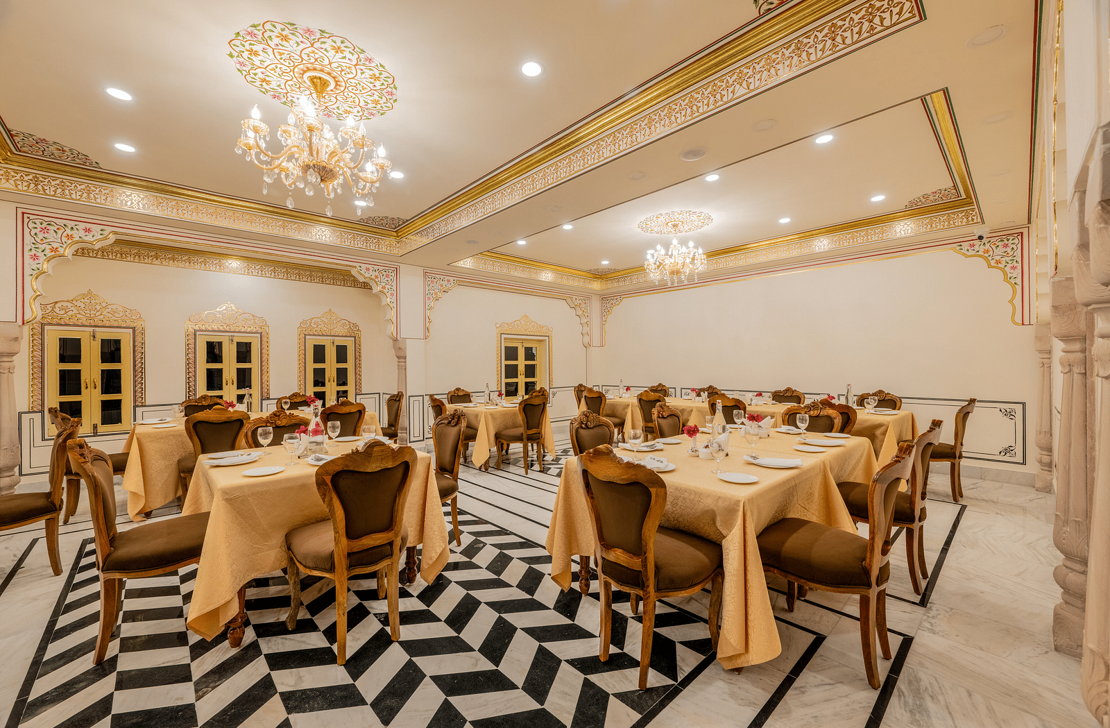 corner view image of the dining area with four windows in the far end of the restaurant and chandeliers hanging from the ceiling - Brij Castle, Jaipur