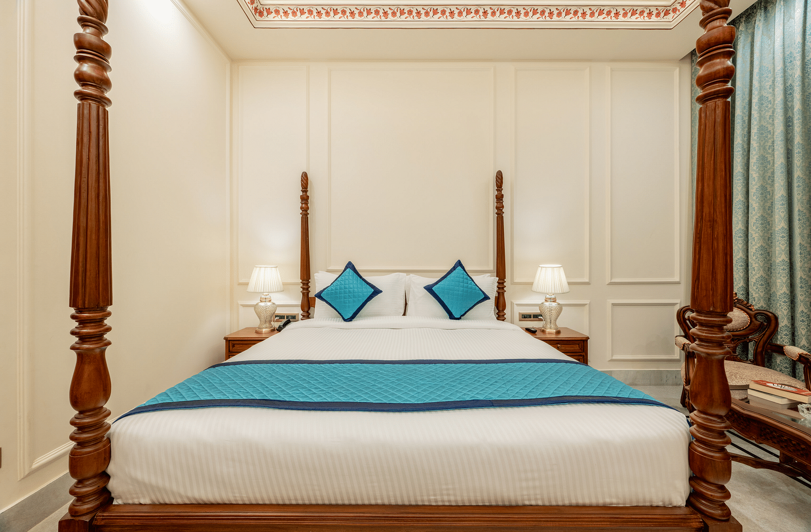full view image of a king size bed with four wooden pillars at each corner of the bed with blue coloured cushions kept on the bed - Brij Castle, Jaipur