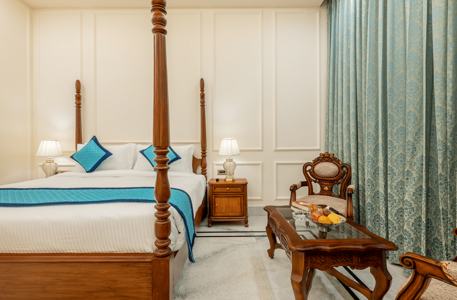 a bedroom with a double bed and a common seating area with a glass top centre table with a fruit bowl in the table - Brij Castle, Jaipur