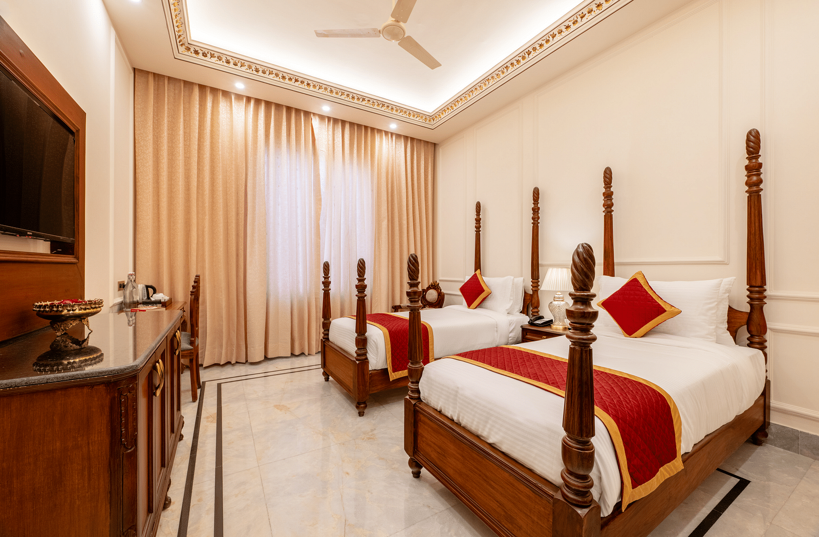 a brightly lit room featuring a twin bed with red coloured cushions - Brij Castle, Jaipur