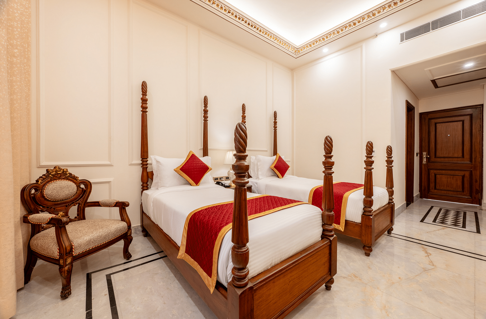 a corner angle of the bedroom with two single beds with a beige coloured cushioned armchair - Brij Castle, Jaipur