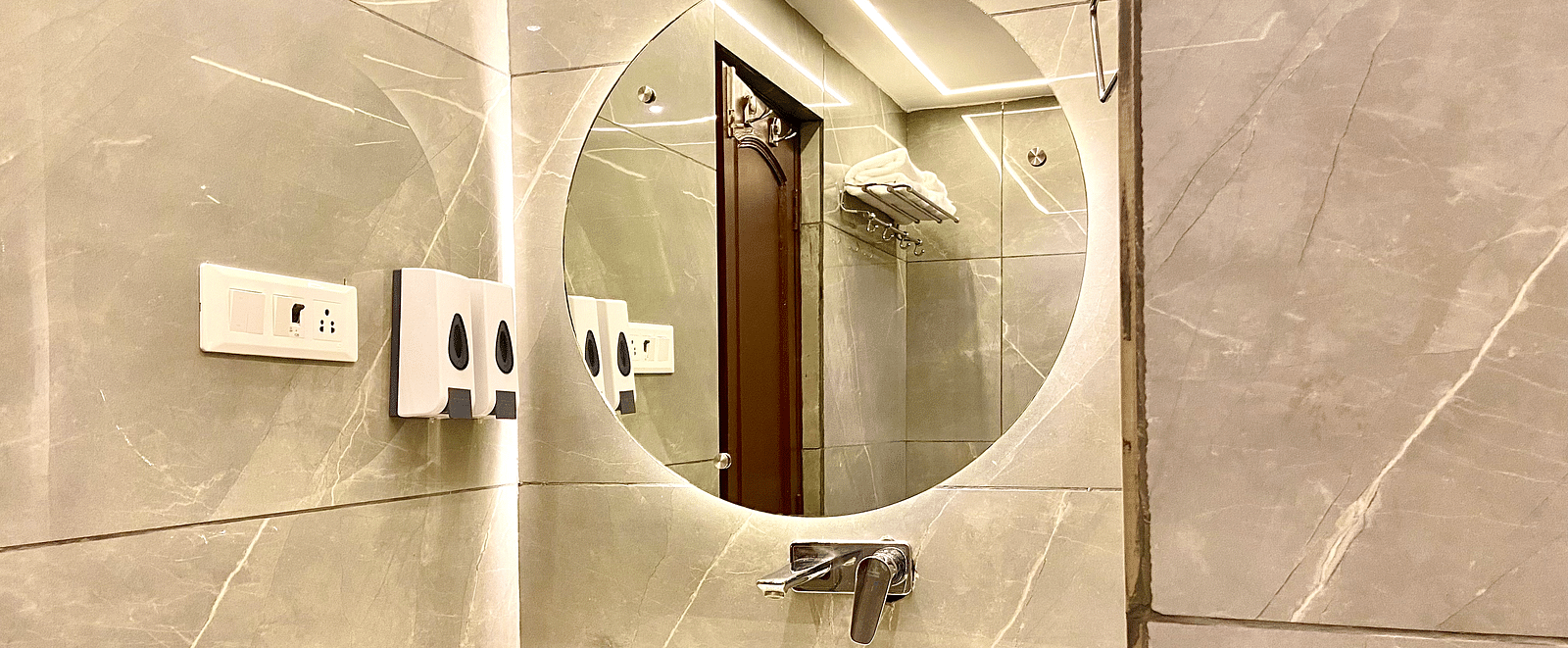 Interior view of a bathroom featuring a circular mirror above the wash basin at DLS Park Grace, Haridwar.