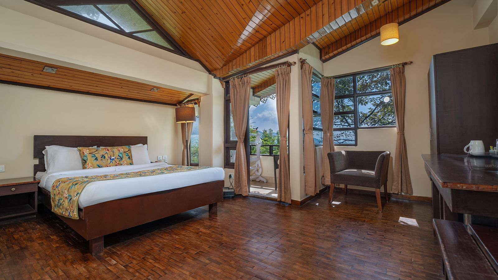 Deluxe room featuring a private balcony, spacious bed, wooden table with cushioned seating, and warm lighting at Summit Norling Resort & Spa, Gangtok