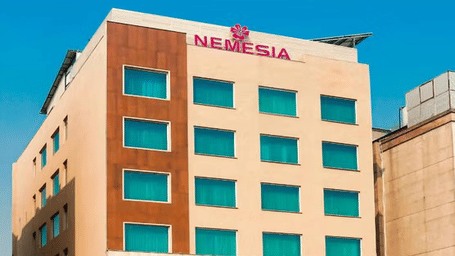 Daytime view of the Nemesia hotel building facade with teal-tinted windows, wooden accents, and palm trees in front.