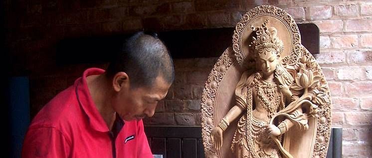 An overview of a man sculpting an idol from wood with accurate hits of the hammer.