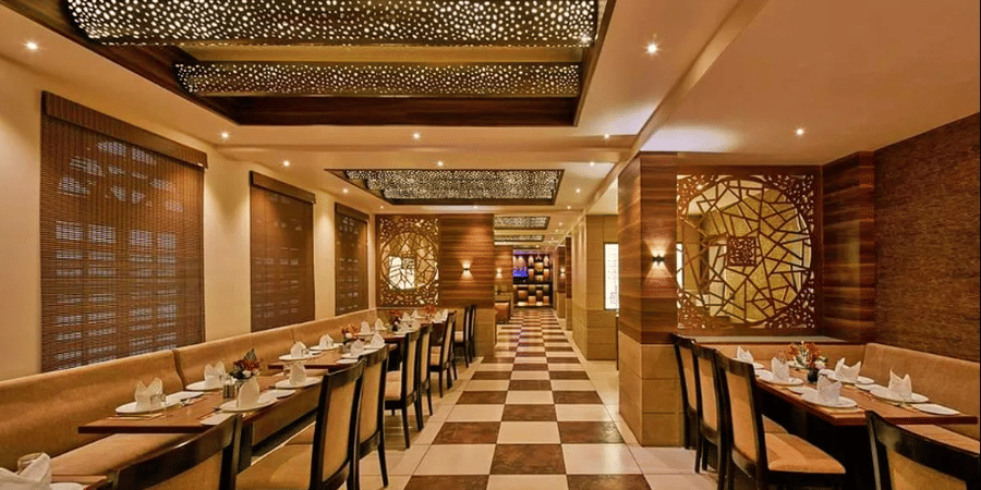 Restaurant interior with long rows of tables, chairs, checkered flooring, and ceiling lights.