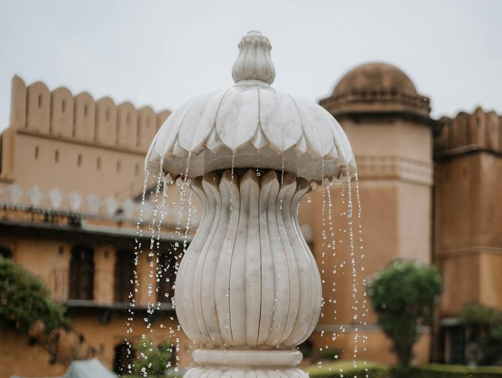 A tiered stone fountain stands prominently in a courtyard with historic buildings in the background.