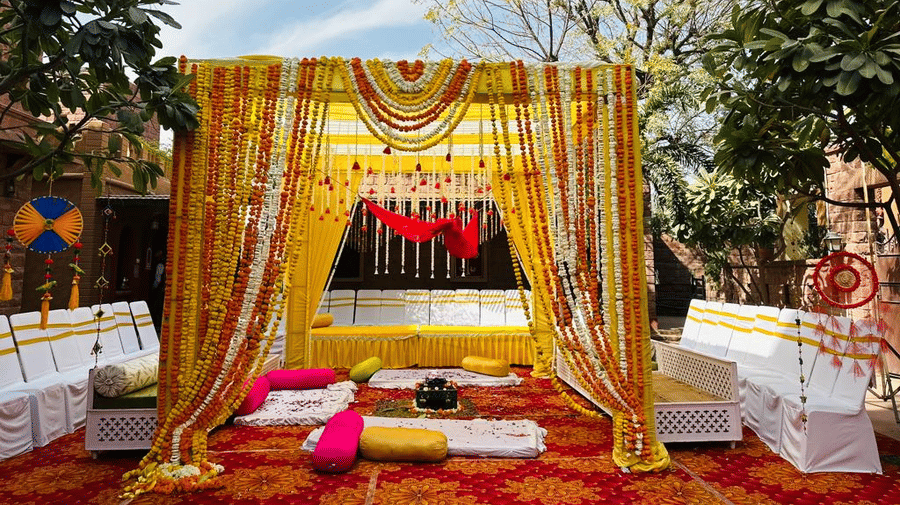 An outdoor mandap decorated with yellow marigold garlands and fabric drapes, next to green trees at Garh Govind.