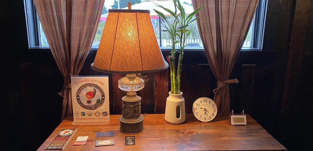 A table in front of a window with a clock, a  table lamp, a indoor plant in a pot are kept