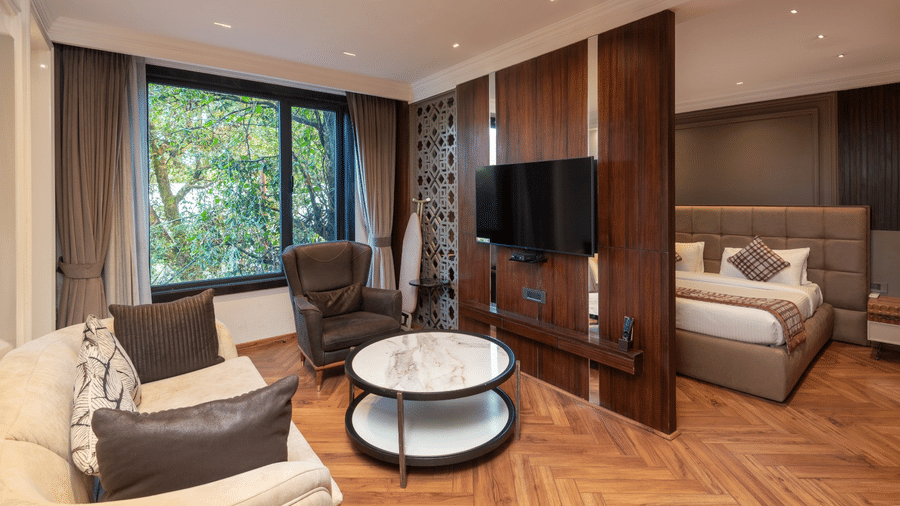 A suite view featuring a flat-screen TV mounted on a wooden wall, a seating area, and a bed in the background | Lawrence Solitaire Resort, Nainital