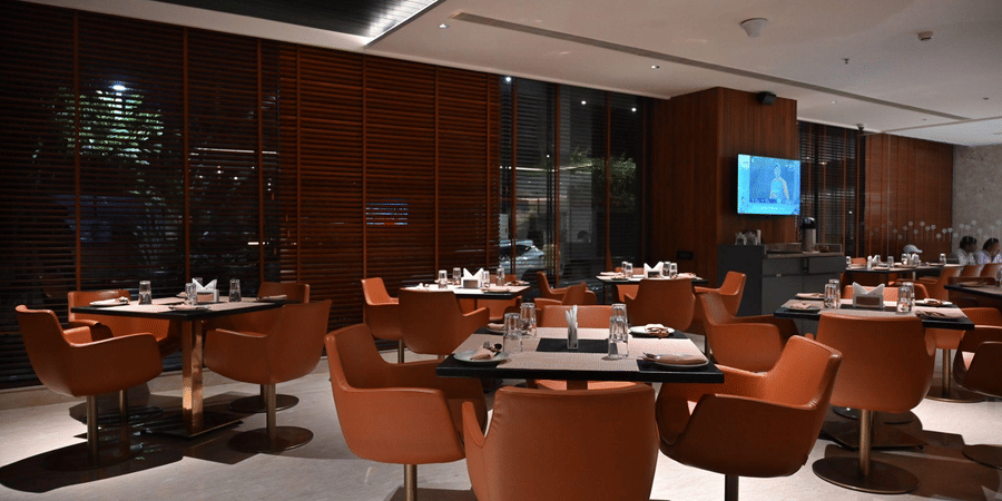 A contemporary dining area with round tables and orange chairs set against a warm, wooden backdrop.