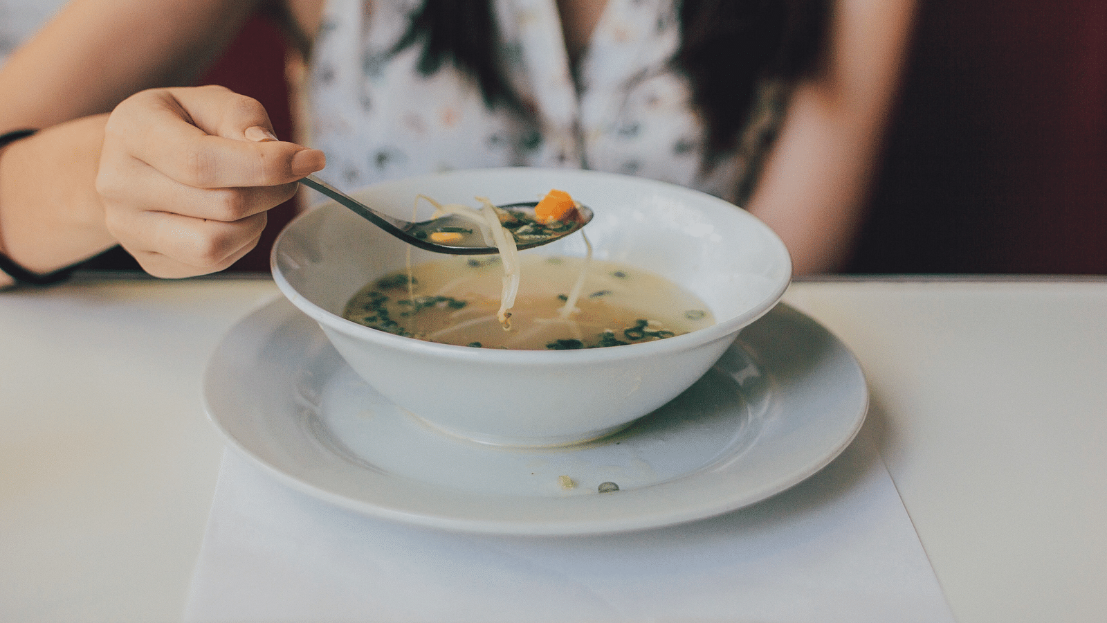 A close up shot of a woman having a shrimp soup served in a bowl.