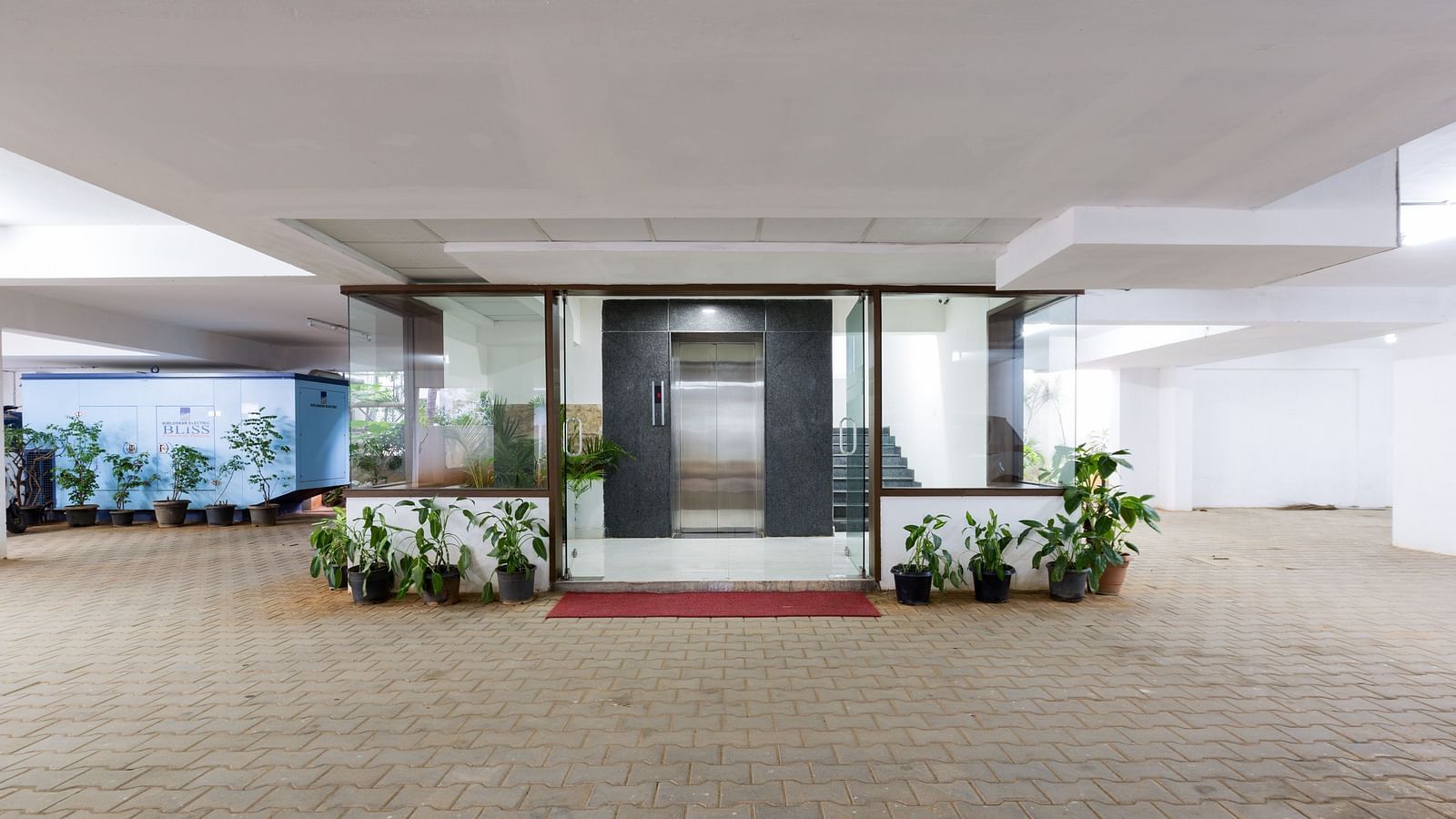 An entrance to a building with potted plants on either sides and an elevator and generator in the background - Sanctum Suites BEL Road, Bangalore