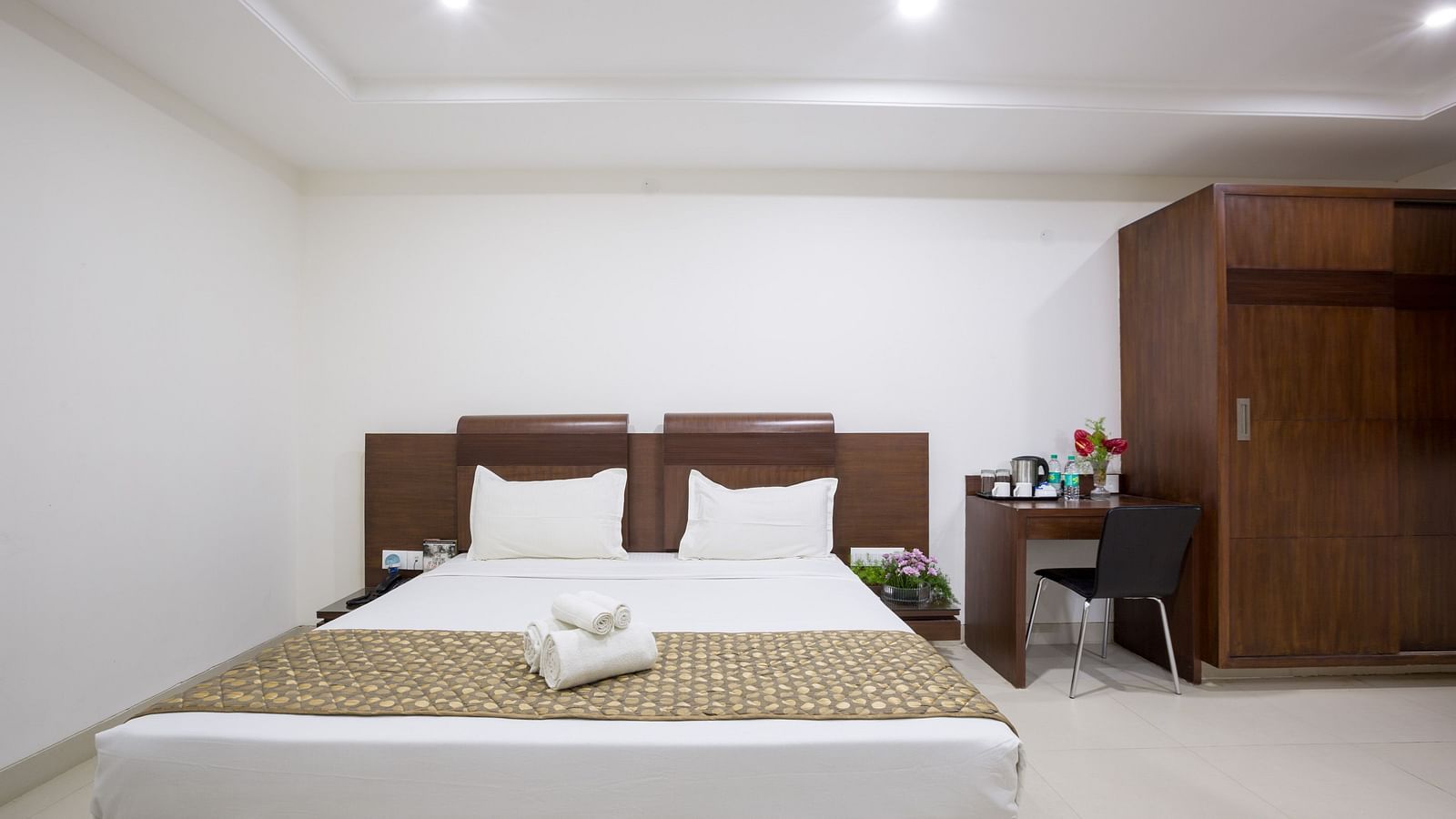 A comfortable room with a bed, bedside tables, and a wardrobe against a white wall - Sanctum Suites BEL Road, Bangalore