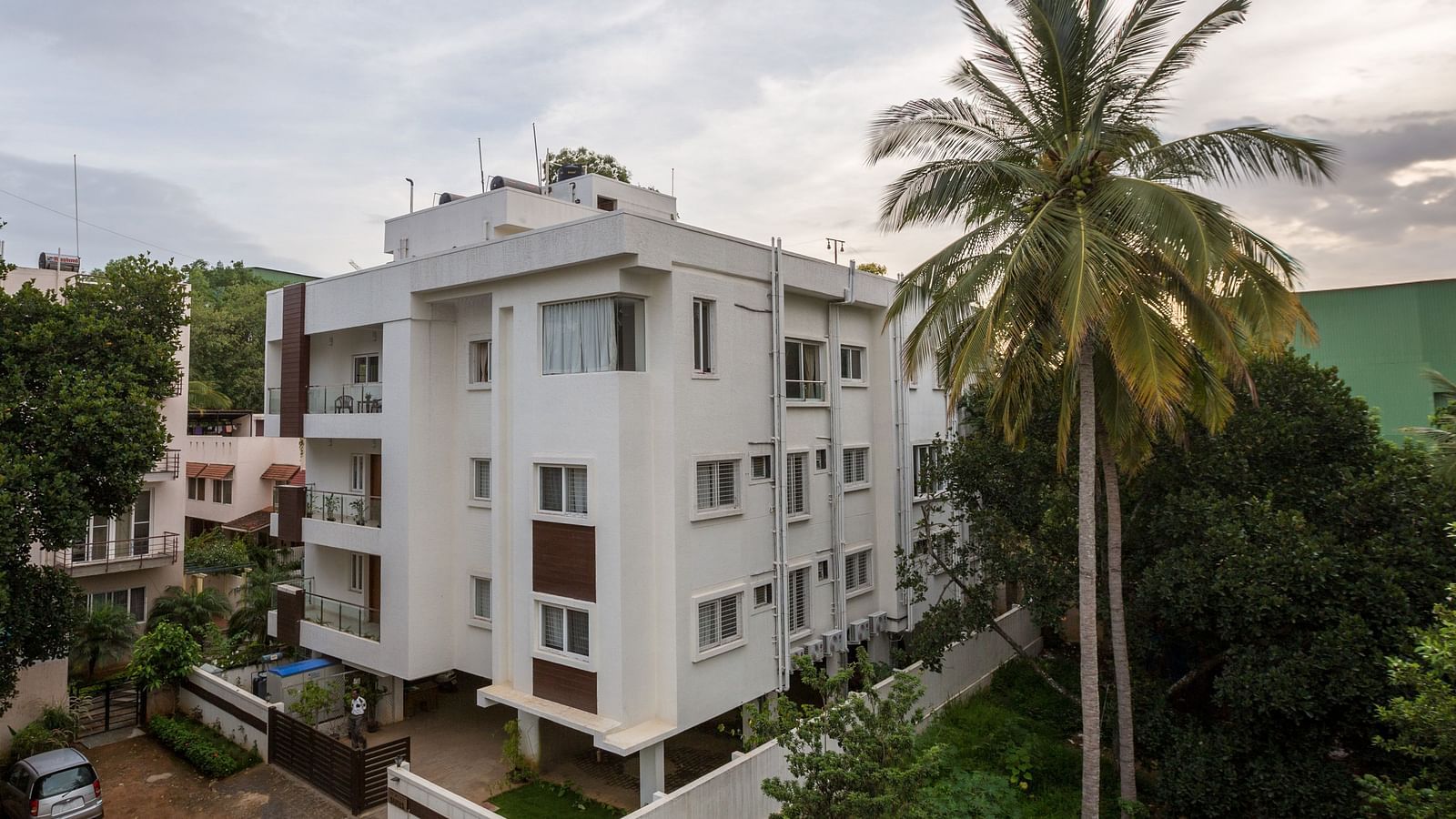 A light-coloured building exterior surrounded by green trees under a bright sky - Sanctum Suites BEL Road, Bangalore
