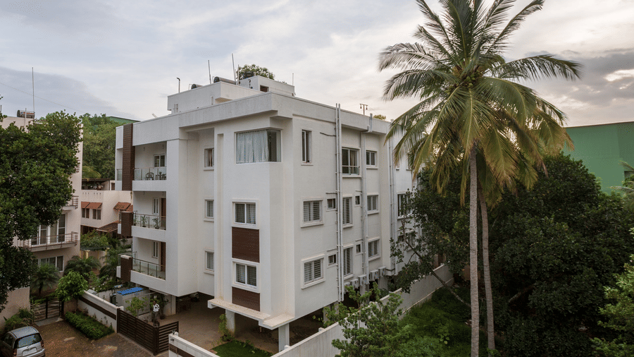 Daytime exterior view of Sanctum Suites building surrounded by palm trees and lush greenery