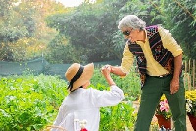 Staff member serving food to a seated guest in the garden area of Karma Chalets during daylight.