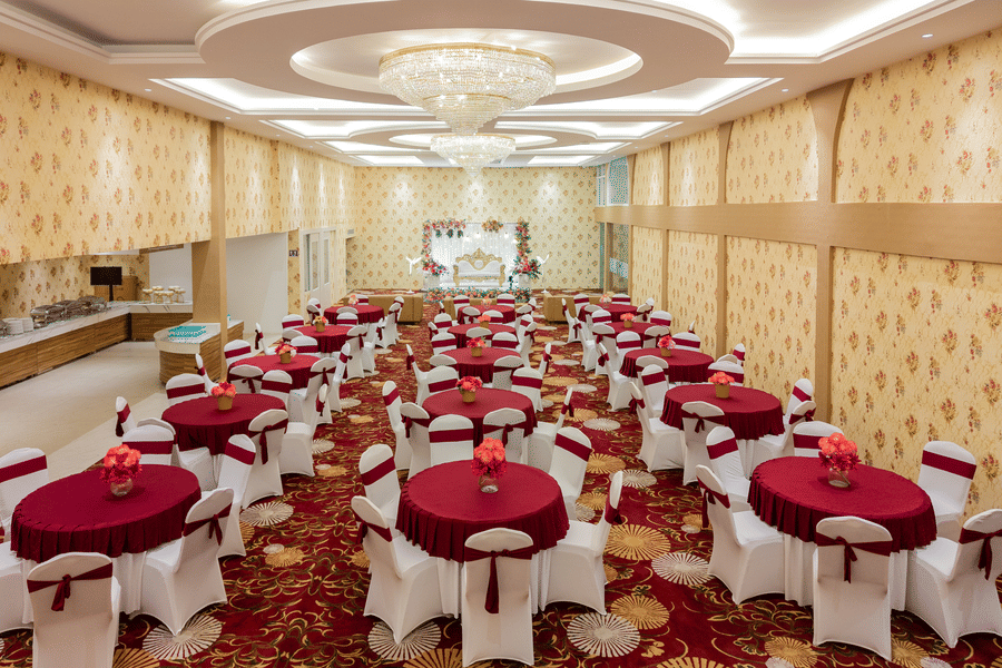 Wide view of banquet hall set up with round tables and red linen at Mango Grove Hotel.