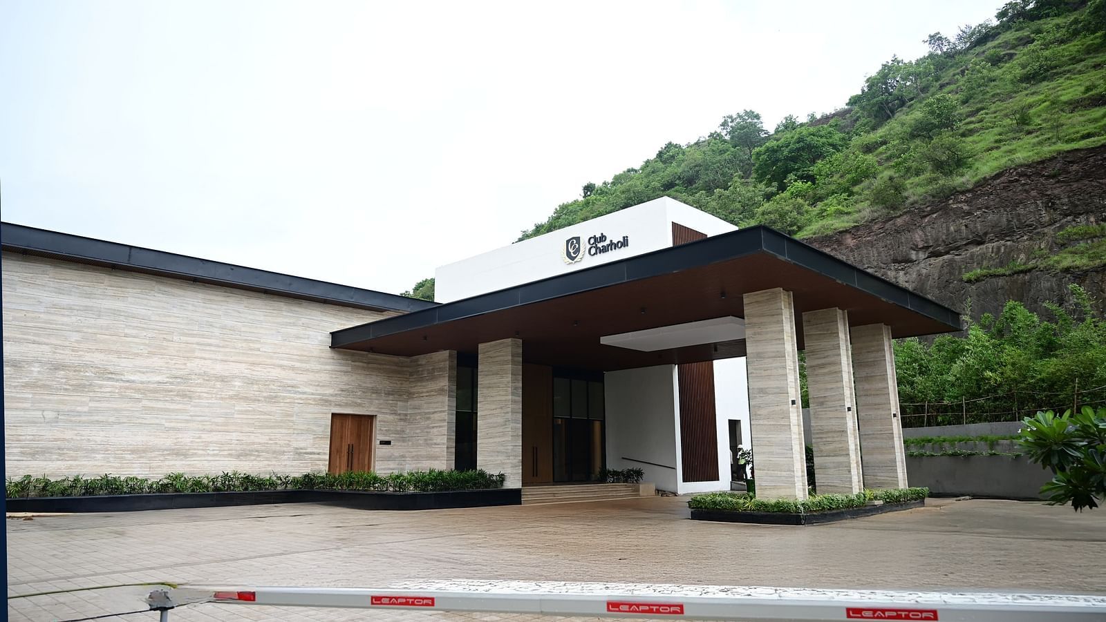 A building entrance with a gate and a hill in the background with lush landscapes - Club Charholi, Pune 