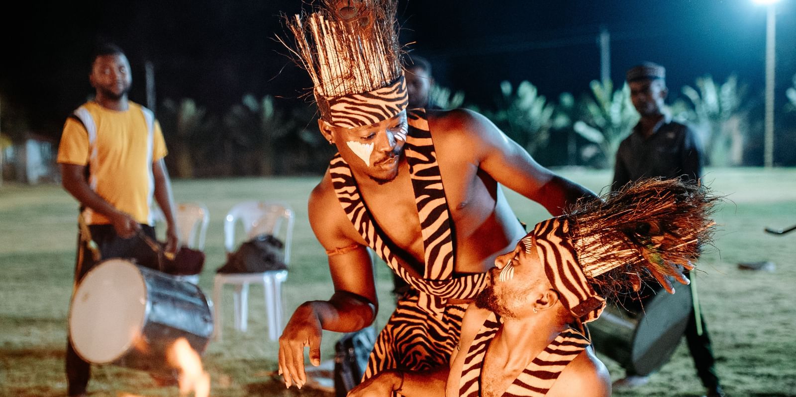 Two people wearing traditional tiger-print outfits and performing while by standers watch -Daksh Eden Greenz, Sasan Gir