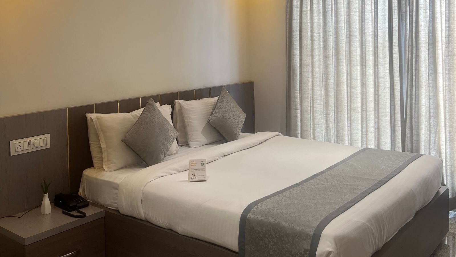 Focus on the double bed in the Daksh Comfort Room at Daksh The Valley Resort, Saputara, seen beside long closed curtains on one side of the room.