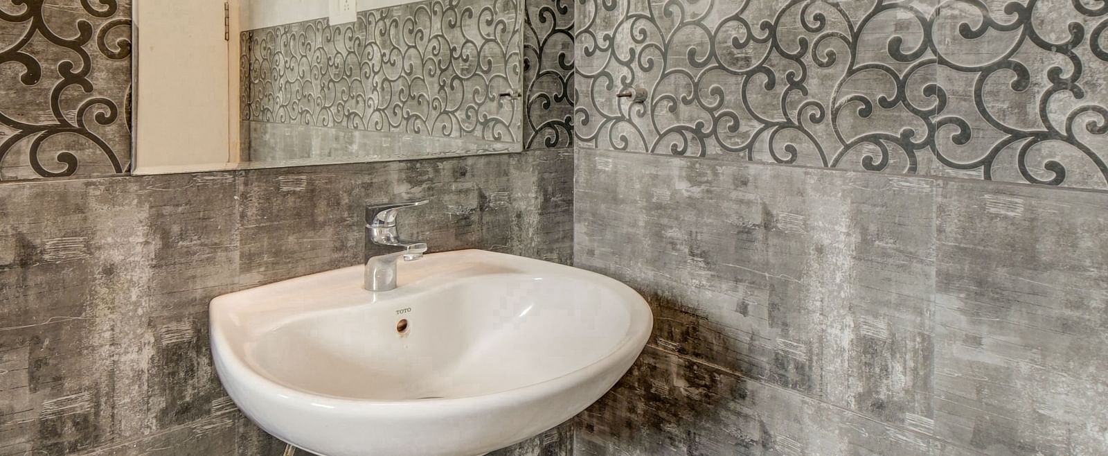 A spacious washroom at Harigovinda's JNStay with a wall-mounted mirror, washbasin below it, and bright lighting