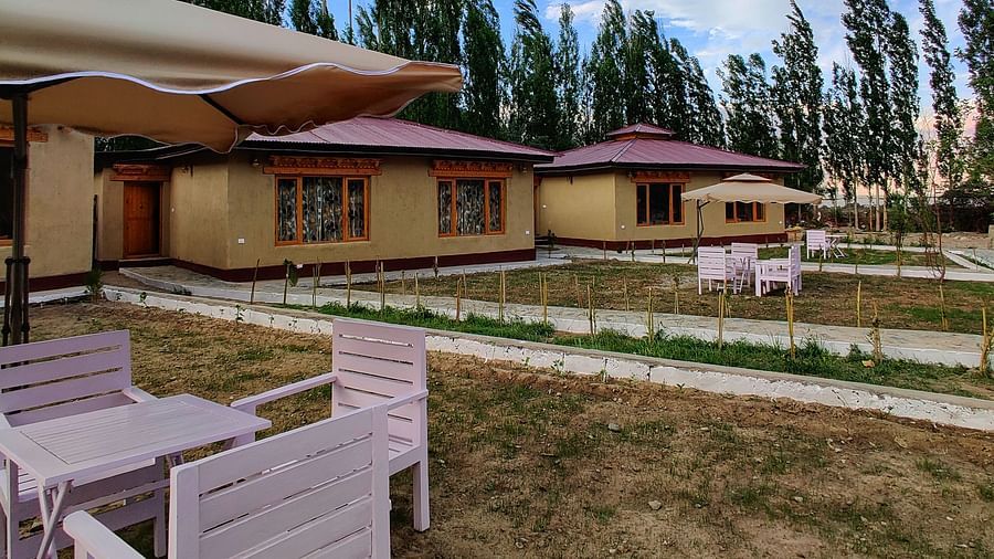 An exterior view of the White Sands Resort, Ladakh showcasing the wooden architecture and surrounding trees under a clear sky.
