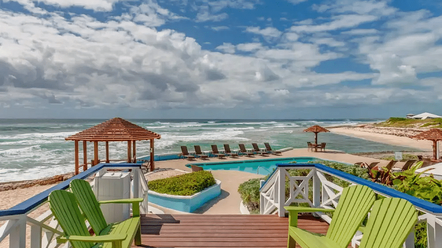 Wooden deck with two bright green chairs facing a turquoise ocean, with a boardwalk and loungers in the distance | Abaco Inn