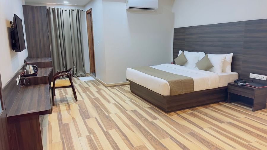 A room displays a double bed, a television, a chair, and wooden flooring - Kankidham Lords Inn