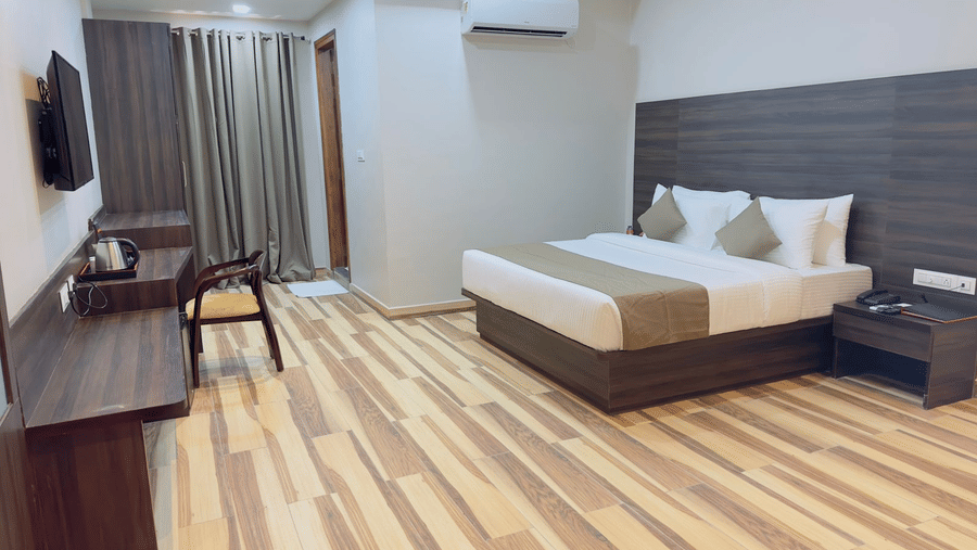 A room displays a double bed, a television, a chair, and wooden flooring - Kankidham Lords Inn