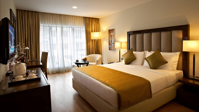 A bedroom featuring double size bed, a flat TV screen, a cabinet, a sofa and centre table, and a few lamps at Adarsh Hamilton