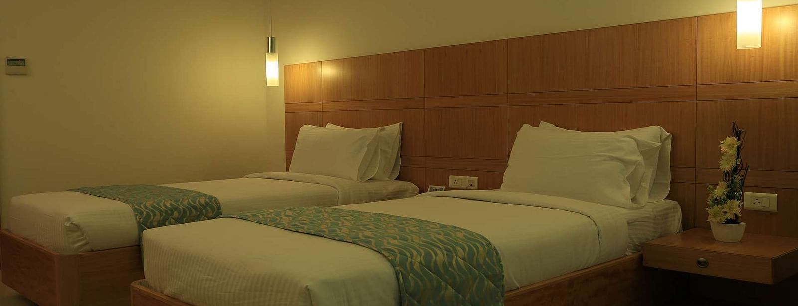 A comfortable twin-bedroom setting with bedside lamps and a soothing ambience for a peaceful night’s rest.- Dhanalakshmi Srinivasan Hotels, Perambalur