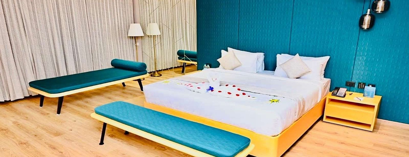 Close up view of a Presedential Suite featuring a King size bed with white linens and decorative swans, a green accent wall, yellow furniture, and hardwood floors - Dhanalakshmi Srinivasan Hotels, Perambalur