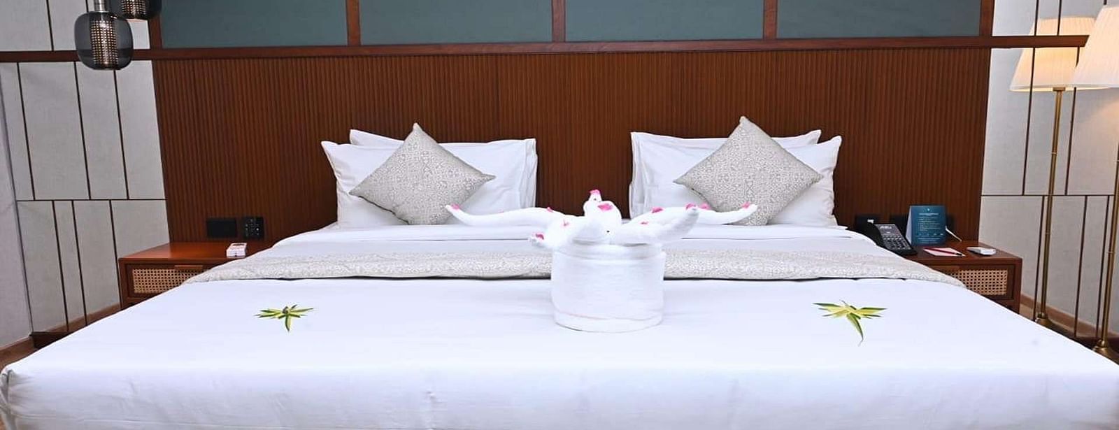 Close up of a Executive Suite at Dhanalakshmi Srinivasan Hotels, Perambalur featuring a bed with white linens, and dark wood headboard