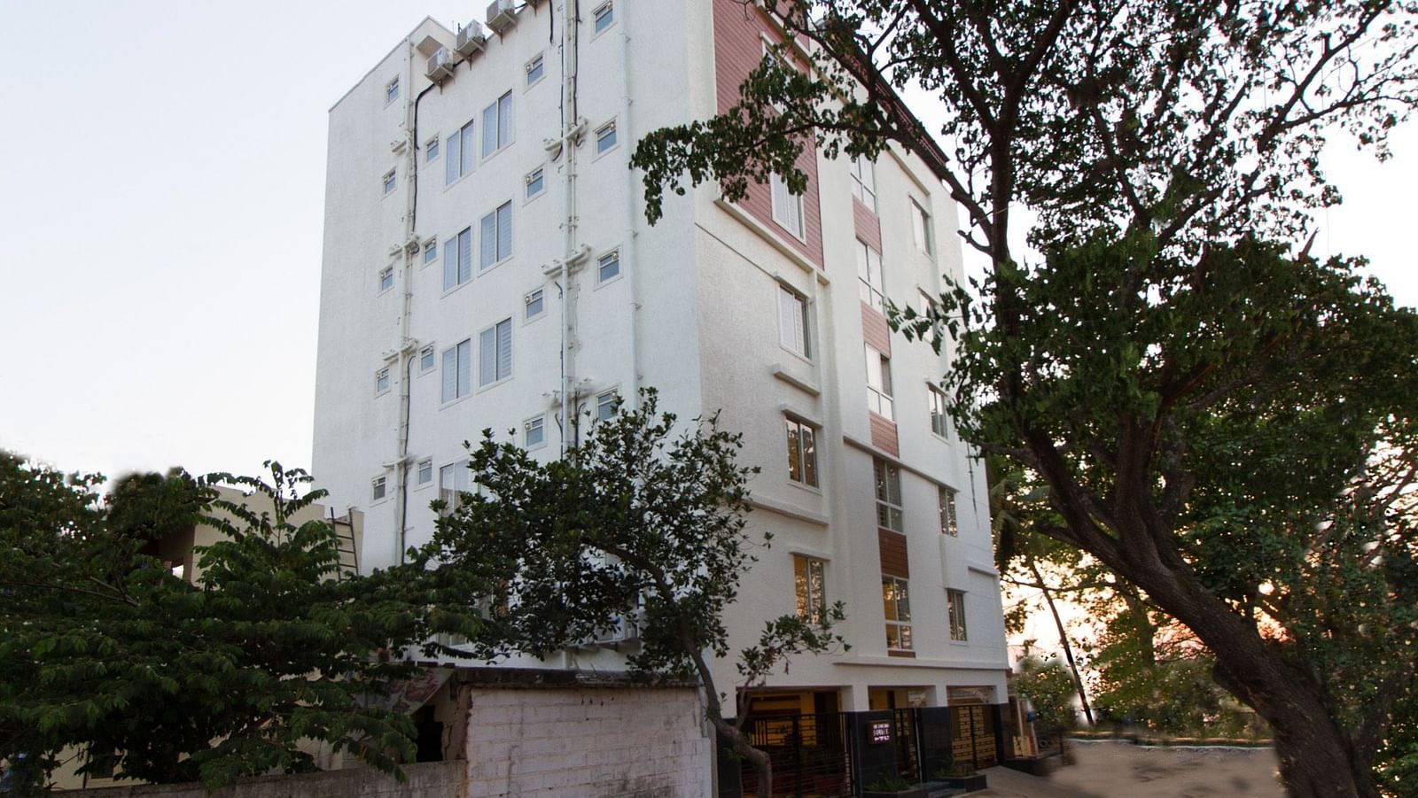 The multi-storey building of Sanctum Suites Whitefield, Bangalore amongst trees under a daytime sky.