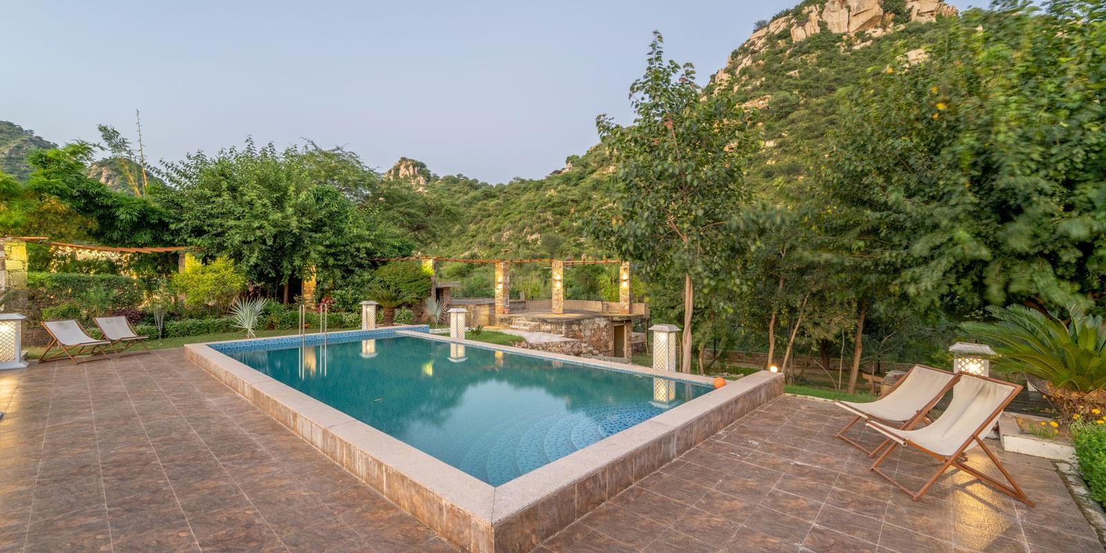 An outdoor pool at Valley by Grassfield, surrounded by plants and trees, with two lounge chairs on the side.