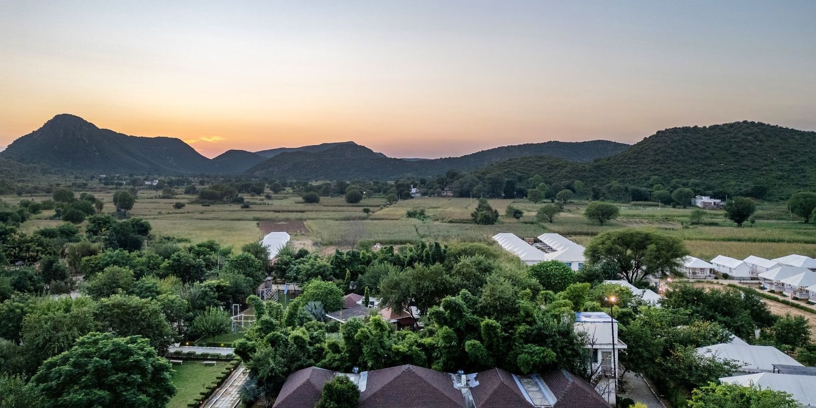 Aerial view of Valley by Grassfield, surrounded by lush greenery with mountains in the background.