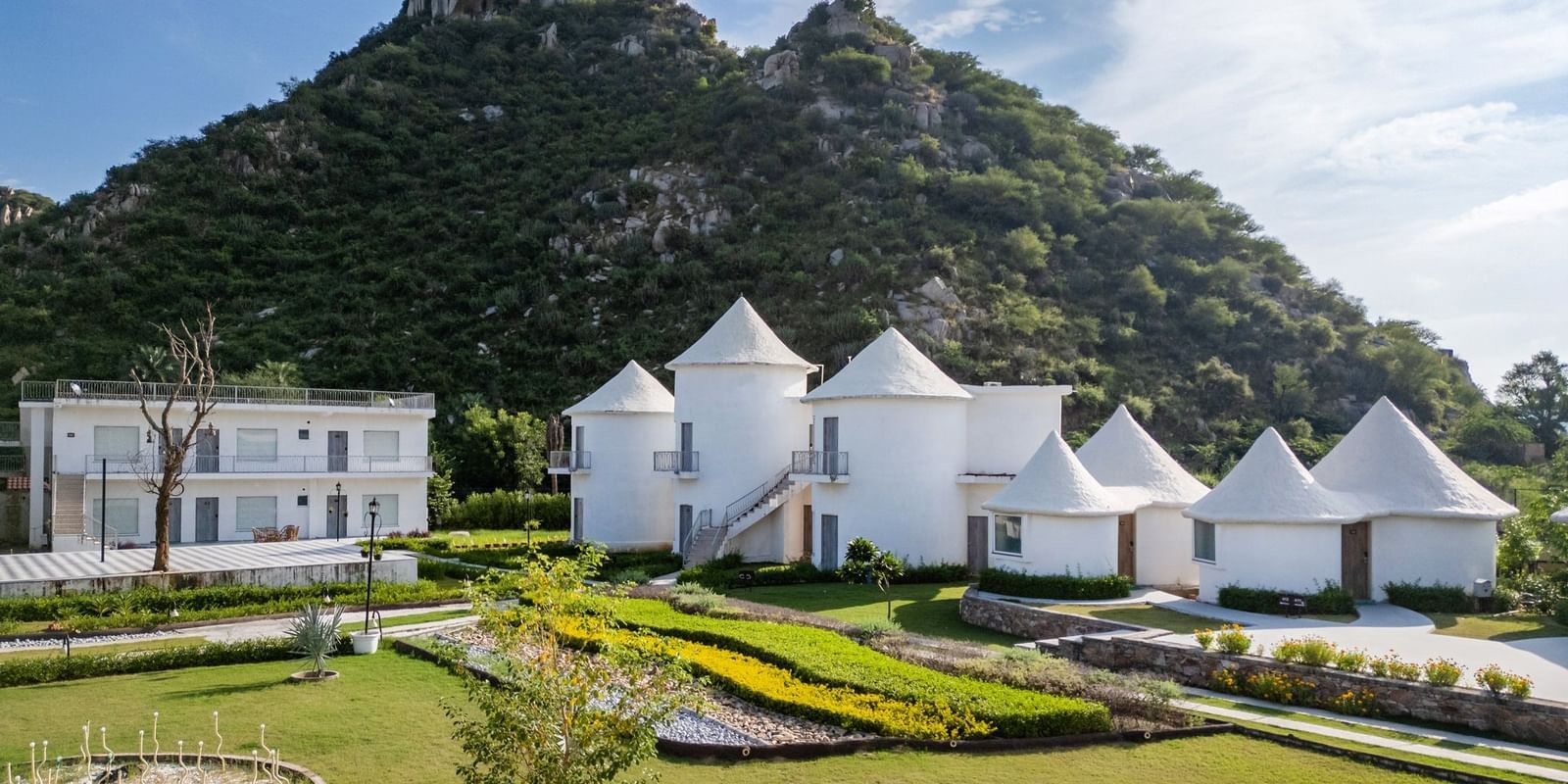 Conical-roof accommodations with an open space in front, set against a scenic mountain backdrop at Valley by Grassfield.