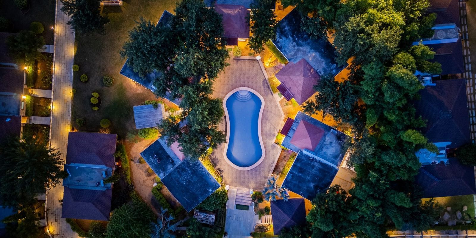 Aerial view of Valley by Grassfield, highlighting the accommodations illuminated by glowing lights, with a swimming pool at the centre.