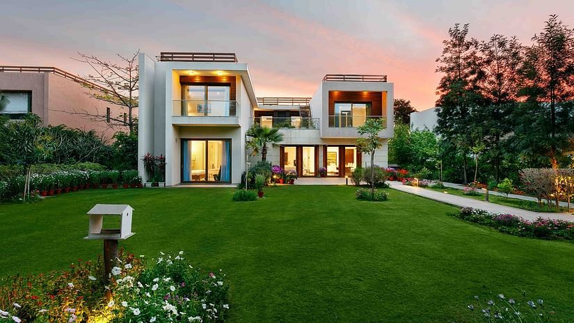 Facade view of the Woodpecker Villa at Karma Lakelands with a green lawn and garden in front.
