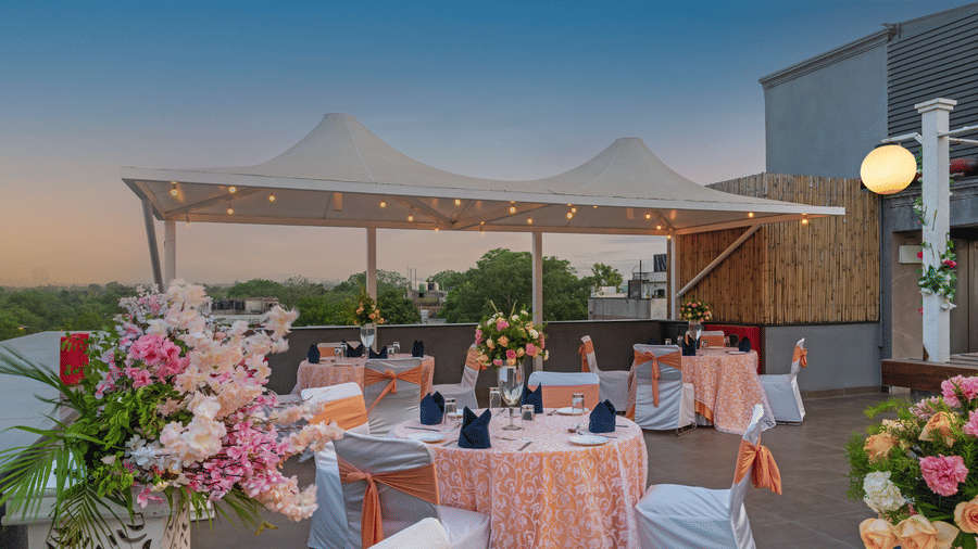  Terrace seating arrangement with round tables, covered canopy, and floral centrepieces at Hotel Saket 27, New Delhi.