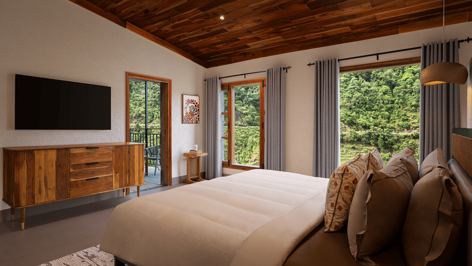 Corner view of a room at Samsara Hill Resort, Mussoorie, showcasing the plush bed facing the wall-mounted television, and glass windows and doors opening to view of the greenery in the surroundings.