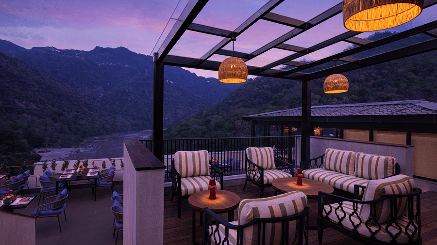 Open air lounge at The Terrace, Aloha on the Ganges, Rishikesh, featuring cushioned seating beneath a pergola with mountain views at twilight.