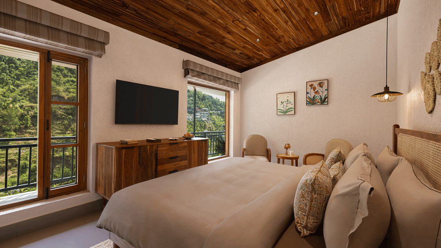 Contemporary bedroom suite with large windows overlooking lush greenery, a wall-mounted TV, and a warm wooden ceiling.